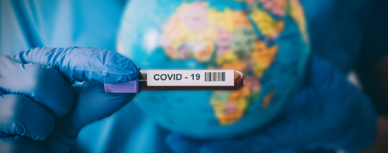 Gloved hand holding vial with blood labeled "COVID-19" in front of globe
