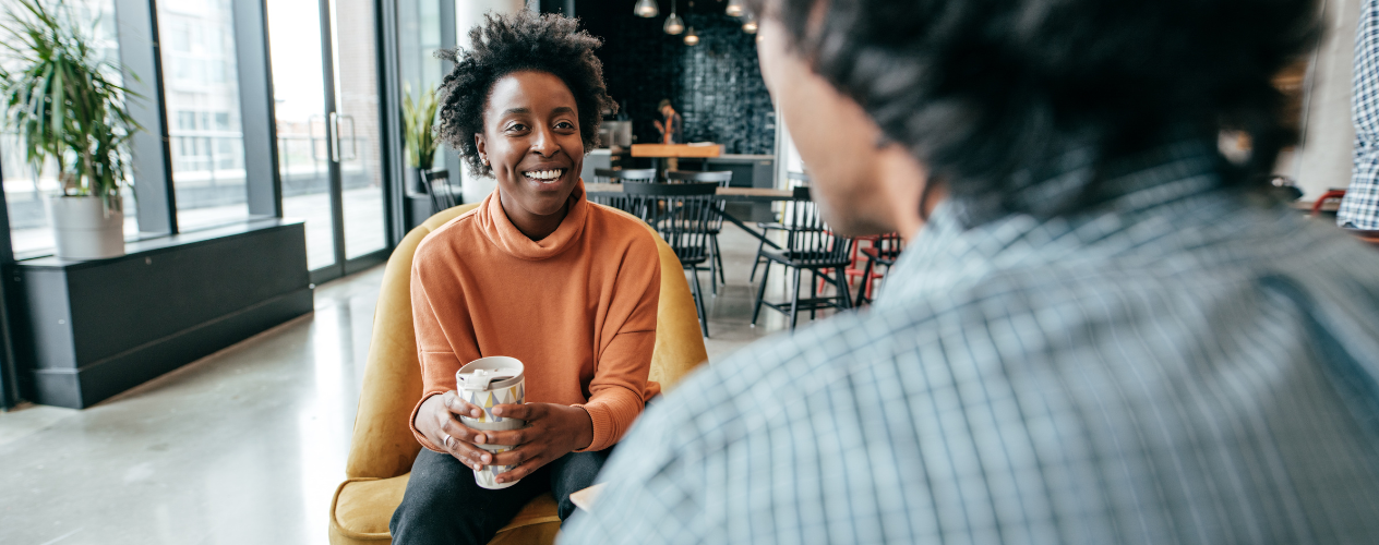 two people sitting in chairs talking and drinking coffee