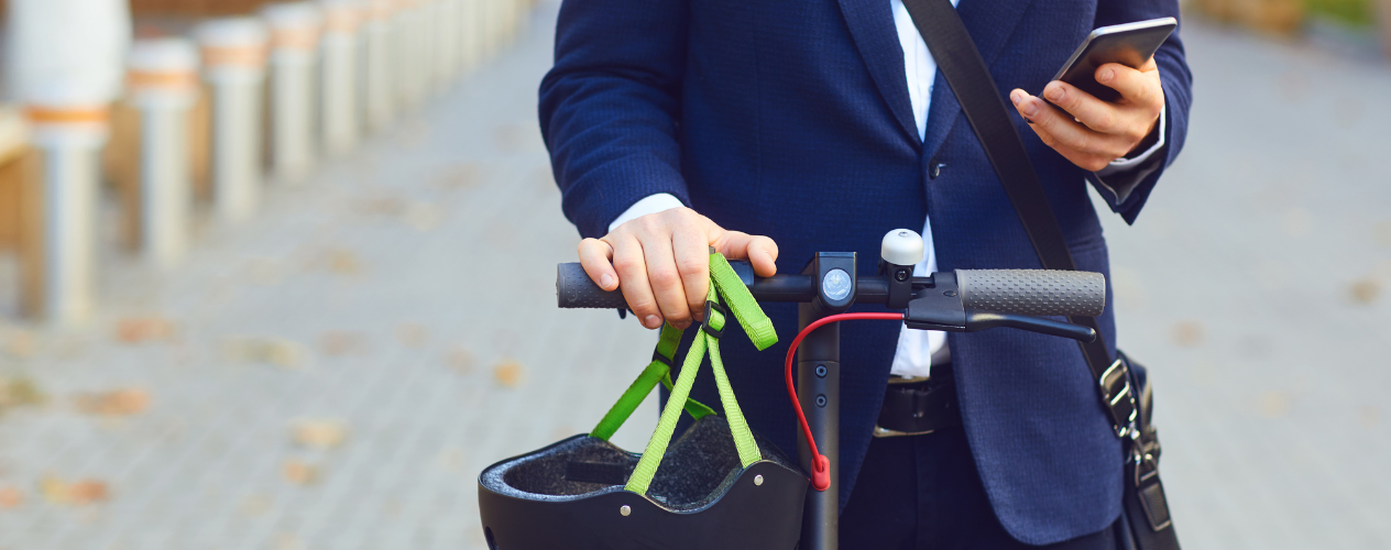 man on e-skooter holding a helmet and looking at his phone