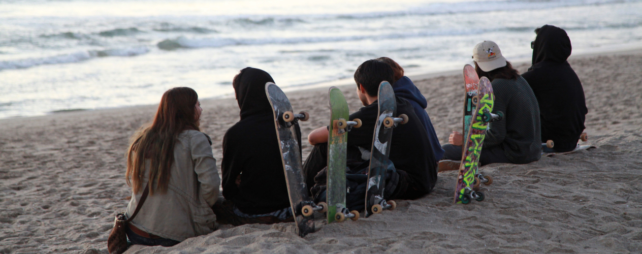 Teenagers with skateboards sitting on a beach