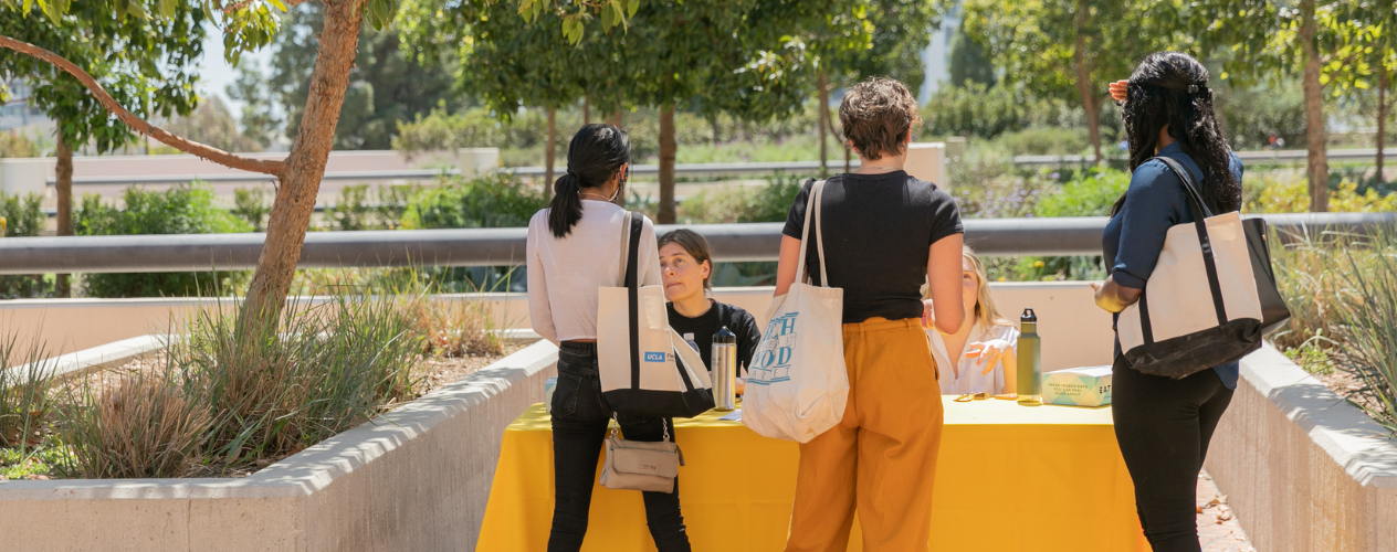 three students standing at table talking to person behind table