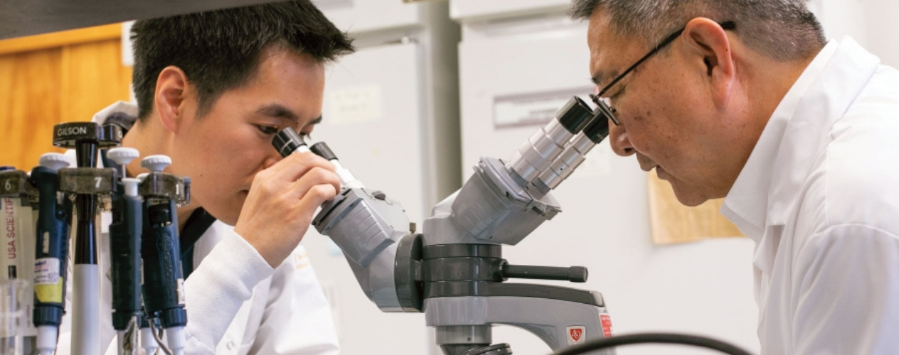 student and professing looking into microscope