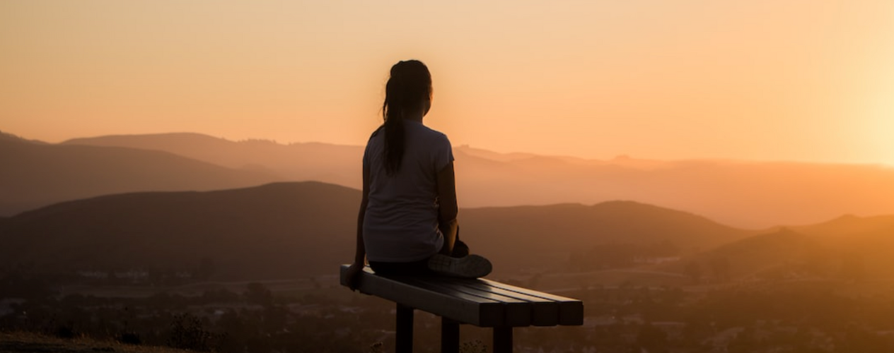 person sitting on bench looking out from top of mountain
