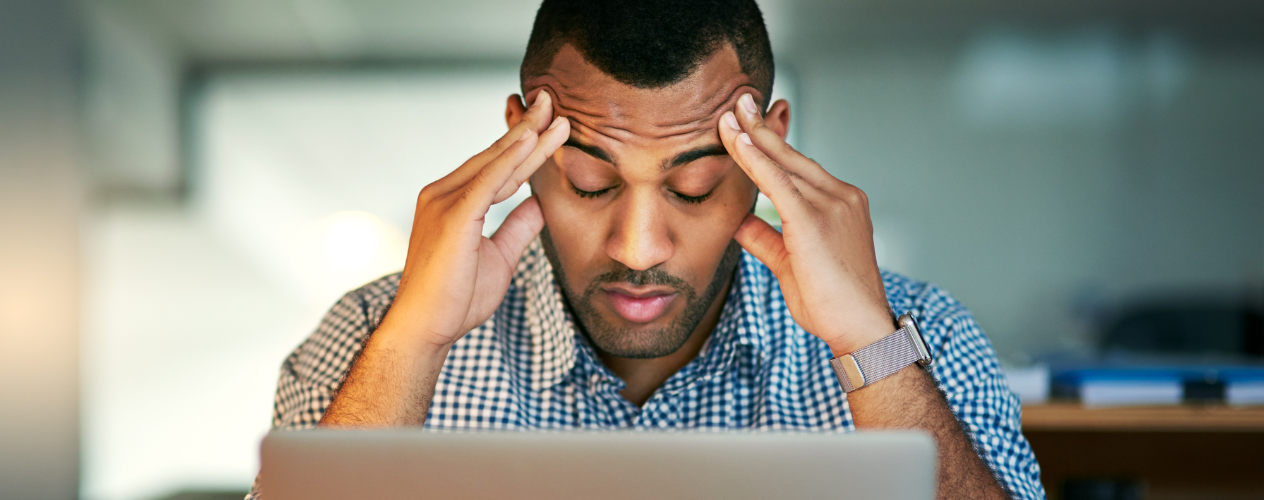 man holding his hands to his head in front of laptop