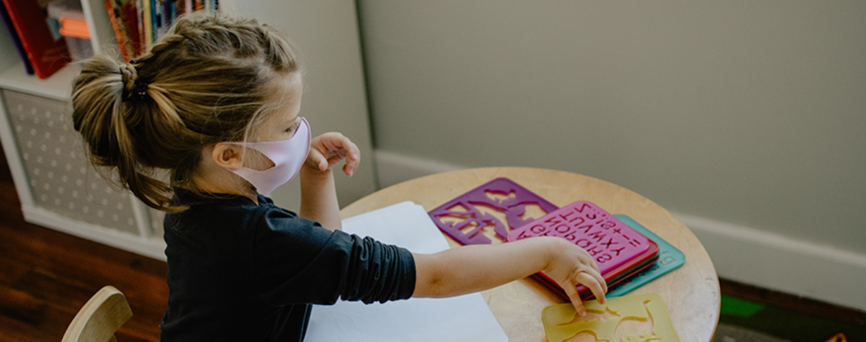 young child in mask coloring