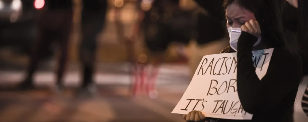 woman crying with sign that says "racism isn't born, it's taught"