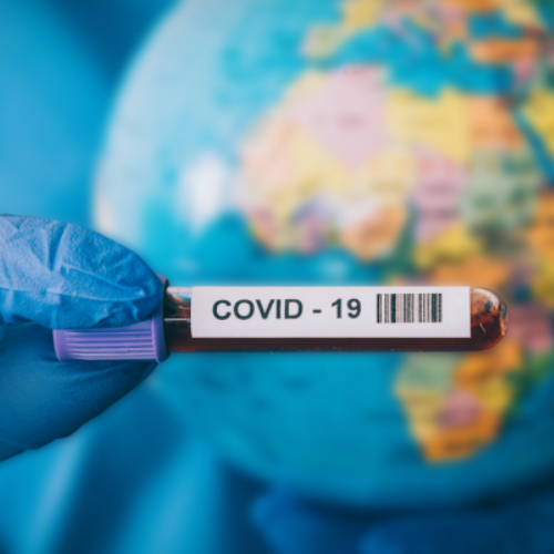 Gloved hand holding vial with blood labeled "COVID-19" in front of globe