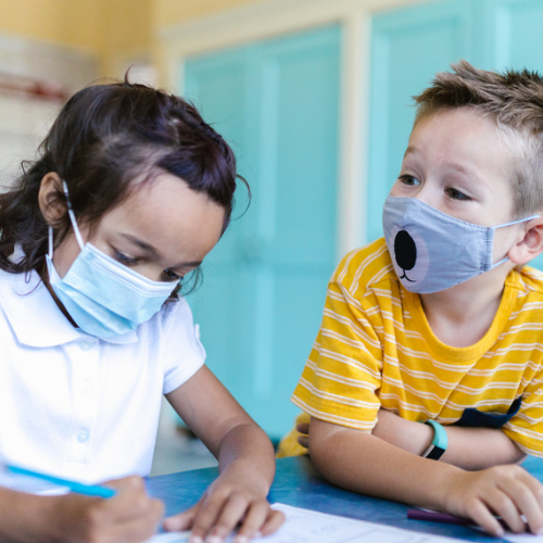 Two elementary students with masks on, sitting at table and working on worksheet