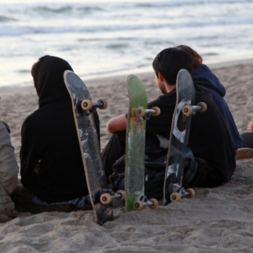 teens sitting on the beach with skateboards