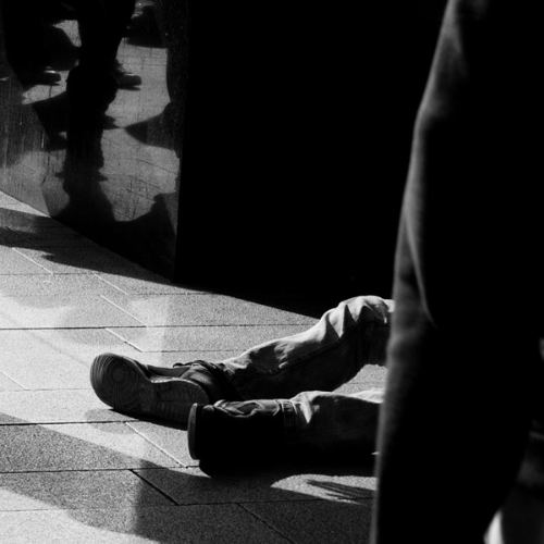 Black and white photo of homeless man's feet and other walking feet