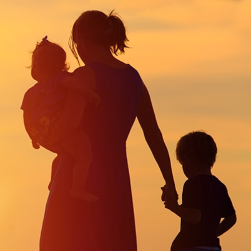 mother carrying a child and holding the hand of another