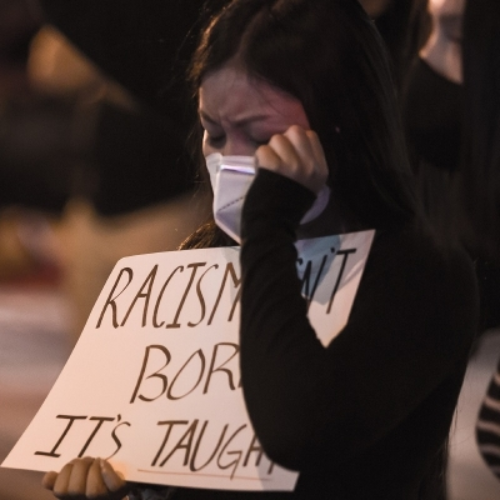 woman crying with sign that says "racism isn't born, it's taught"