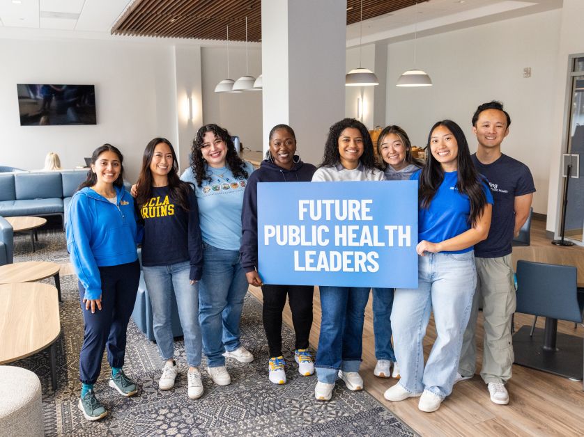 Eight UCLA Fielding students stand together in a campus lounge, holding a blue sign that reads, “Future Public Health Leaders.”