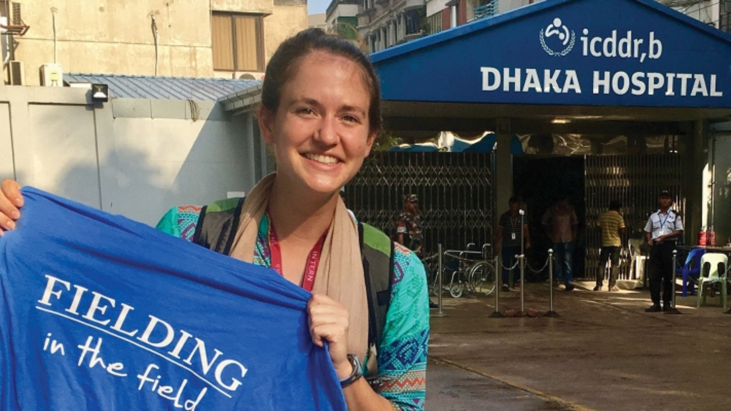 student in front of hospital holding Fielding in the Field tshirt